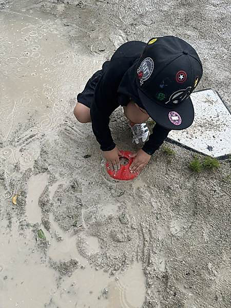 A child crouching in the rain to scoop mud with a cone during outdoor play
