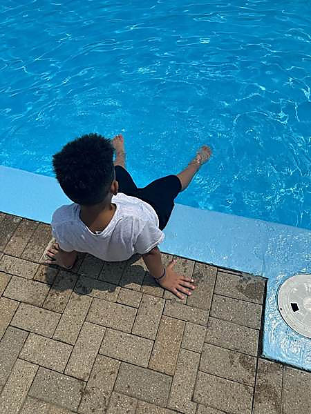 A child sitting on the edge of the pool with their feet in the water