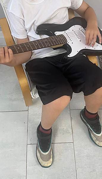 A child sitting with an electric guitar, working out a chord