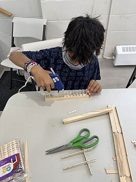 A child using a glue gun to build a wooden loom at the Hexagon maker table