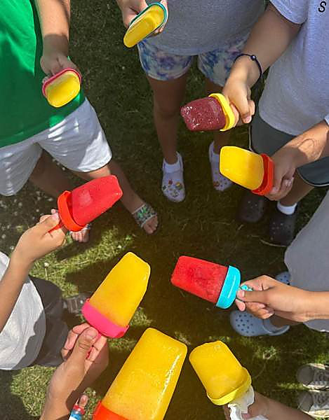 A circle of kids holding up homemade smoothie popsicles on the grass