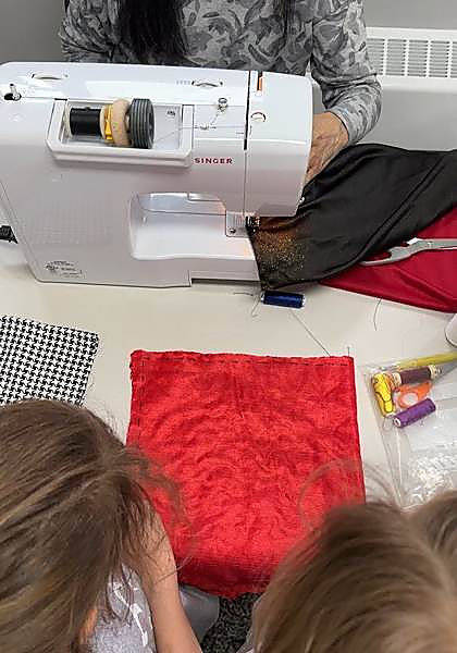 A guide sewing a patch on a machine while two kids watch closely
