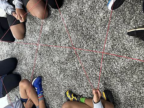 A web of red string stretched between kids sitting in a circle during an icebreaker