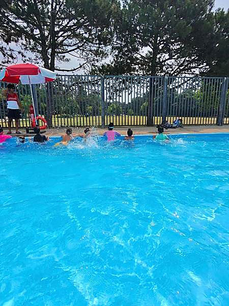 Campers splashing in the shallow end of the outdoor pool with a lifeguard on deck