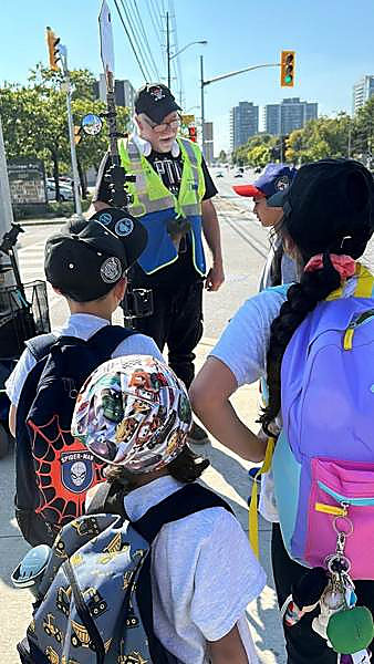 Kids in helmets and backpacks talking with a crossing guard on a neighbourhood walk