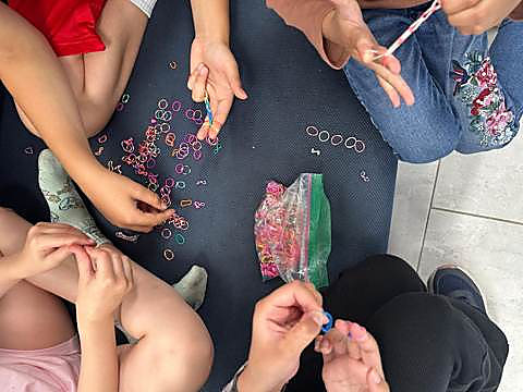 Kids sitting on the floor weaving loom band bracelets from a pile of elastics