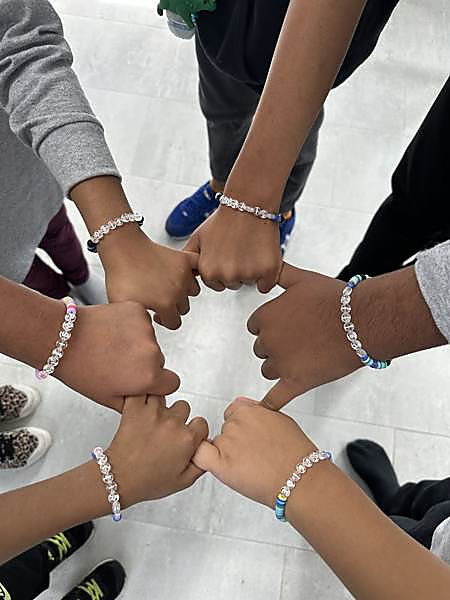 Six kids putting their fists together in a circle, each wearing a bracelet they made